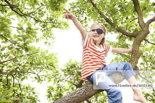 Mädchen verkleidet als Piratin auf einem Baum sitzend  mit dem Finger zeigend