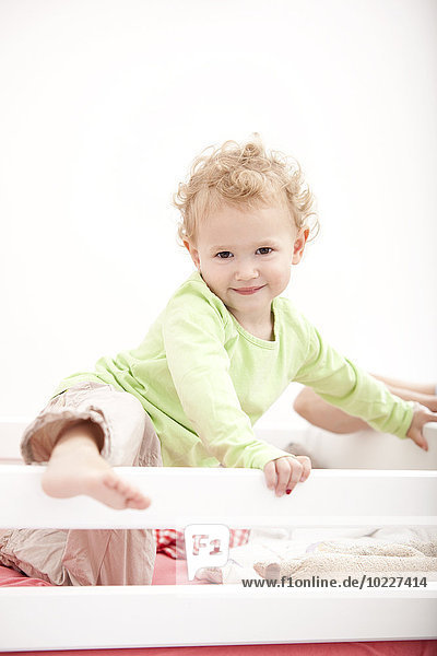 Porträt des kleinen blonden Mädchens im Kinderbett stehend