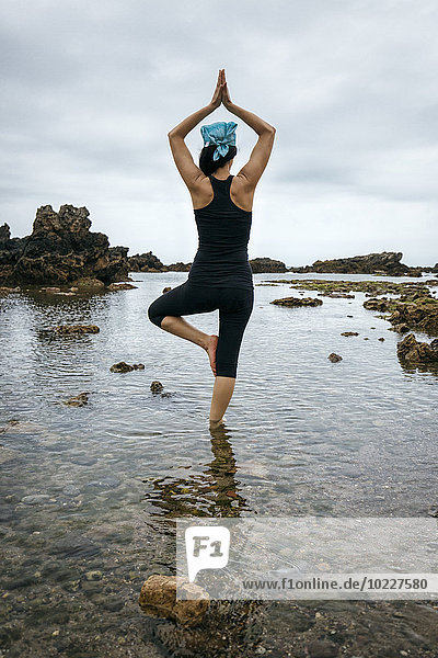 Spain  Asturias  Gijon  woman doing yoga on a rocky beach