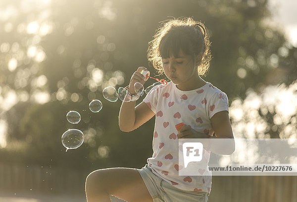 Kleines Mädchen  das in der Dämmerung Seifenblasen im Park macht.