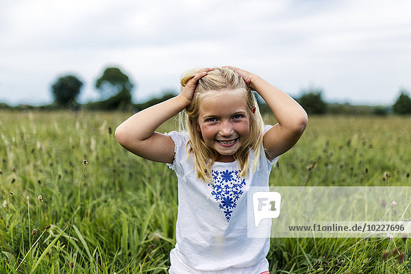 Portrait of smiling girl with hands in her hair on a meadow