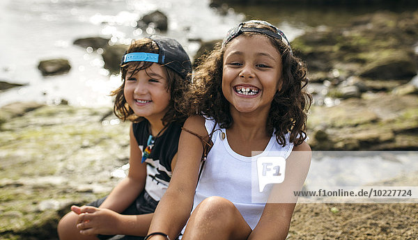 Spanien  Gijon  Porträt des lächelnden Mädchens und ihrer Freundin im Hintergrund an der Felsenküste