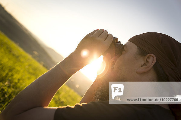 Deutschland,  Mann schaut bei Sonnenaufgang durchs Fernglas