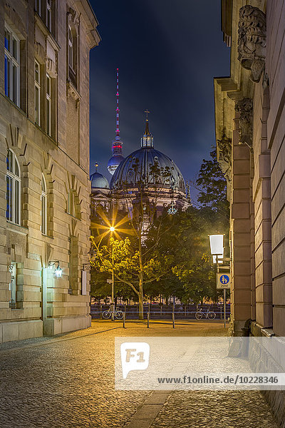 Deutschland  Berlin  Berliner Dom und Fernsehturm bei Nacht durch eine schmale Straße gesehen