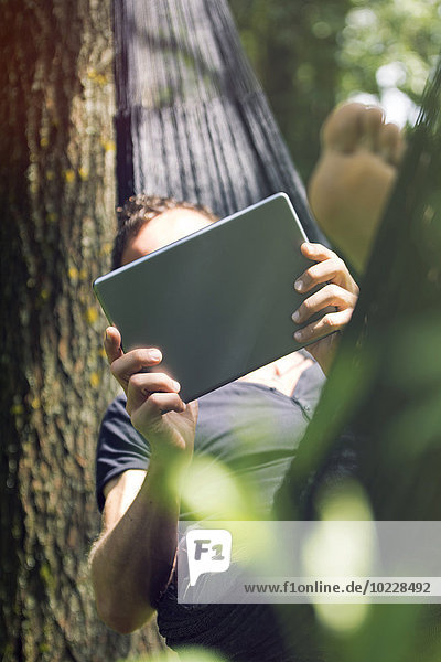 Entspannter Mann in der Hängematte liegend mit digitalem Tablett