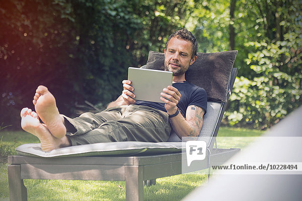Entspannter Mann in der Sonnenliege im Garten mit Digital-Tablett