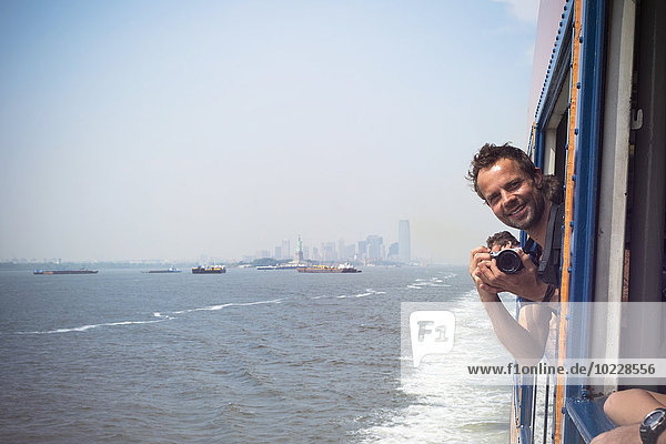 USA  New York City  Tourist with camera on Staten Island Ferry with view of Manhattan skyline and East River