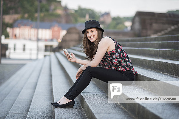Germany  Koblenz  Deutsches Eck  young woman with cell phone sitting on stairs