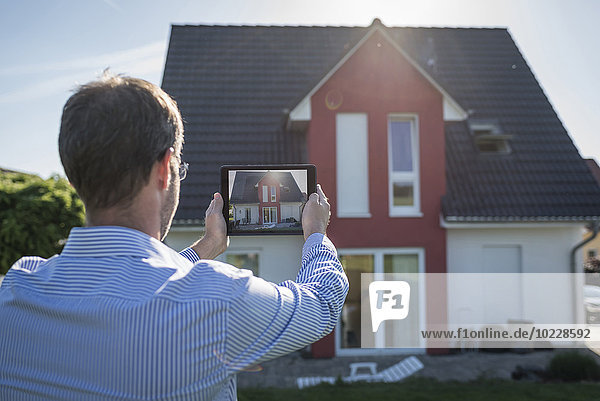 Man photographing his house with digital tablet