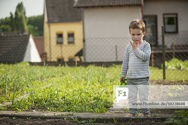 Nachdenklicher kleiner Junge im Garten stehend mit Kindergießkanne