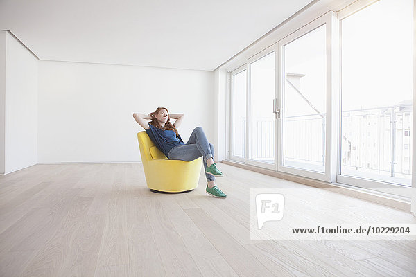 Young woman sitting on yellow armchair in her empty living room