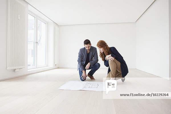 Young couple sitting on floor of their new flat  looking at ground plan