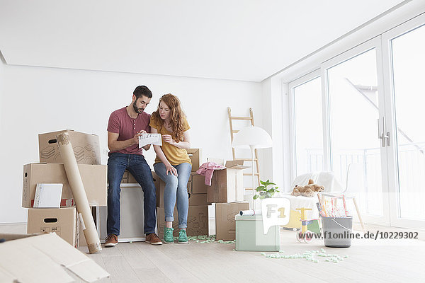 Young couple in new flat with cardboard boxes looking at ground plan