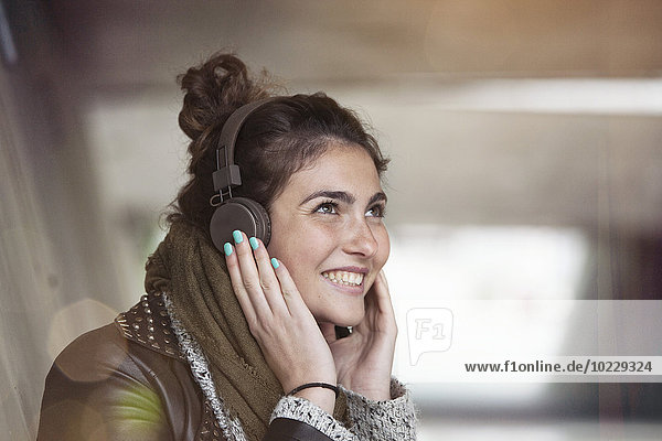 Porträt einer lächelnden jungen Frau  die Musik mit Kopfhörern hört.