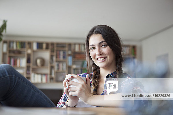 Porträt einer lächelnden jungen Frau mit Kaffeetasse zum Entspannen zu Hause