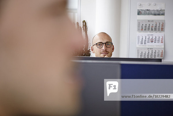 Zuversichtlicher Mann im Büro hinter Computerbildschirmen