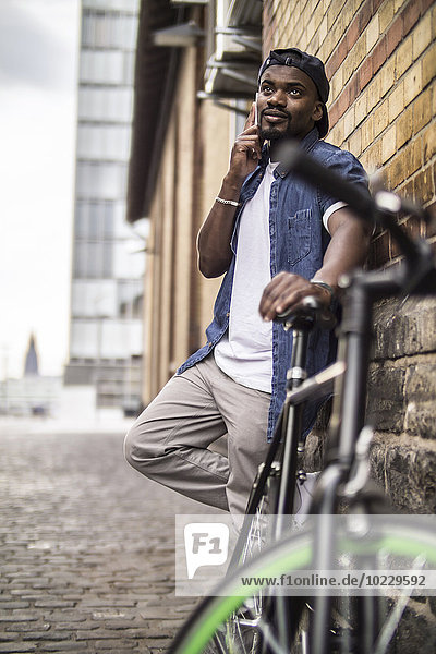 Germany  Cologne  portrait of young man with bicycle telephoning with smartphone