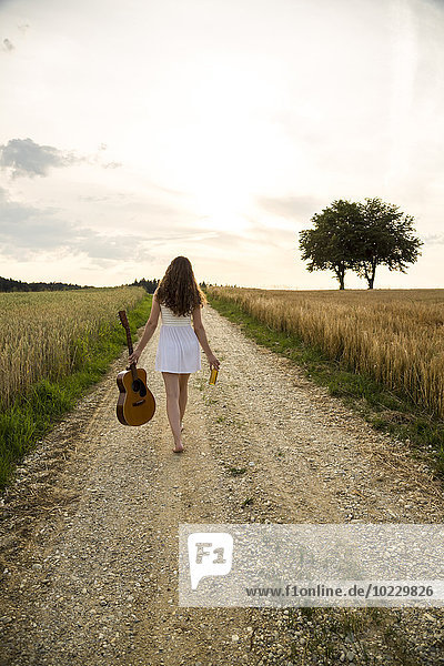 Young woman with guitar on field path  in the evening
