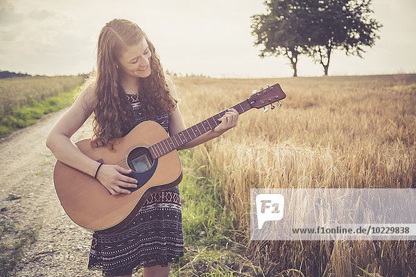 Junge Frau spielt Gitarre  Feld am Abend