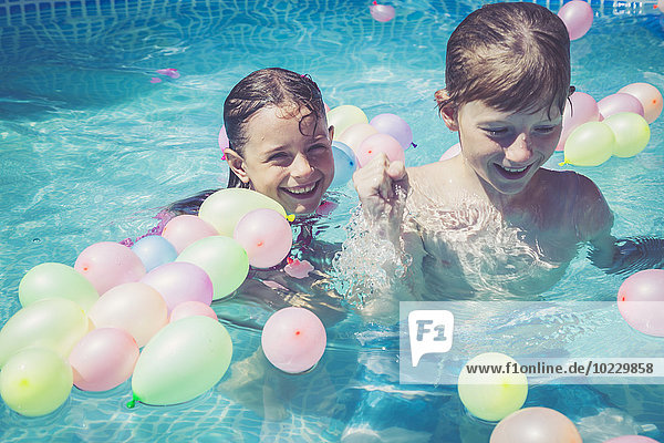 Glückliche Jungen und Mädchen im Schwimmbad  umgeben von Luftballons.