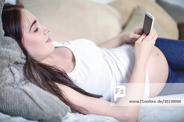 Pregnant woman relaxing on the couch using smartphone
