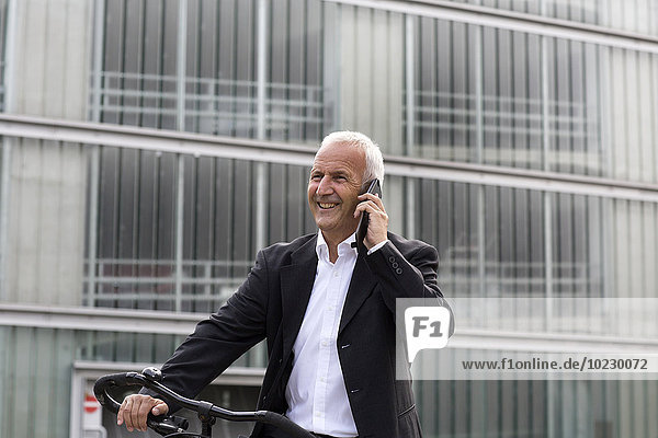 Businessman with bicycle telephoning with smartphone