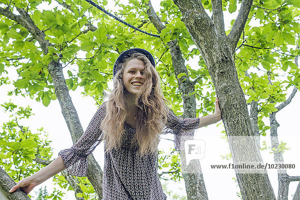 Porträt einer lächelnden jungen Frau  die auf einen Baum klettert.