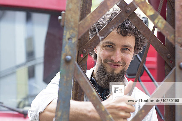 Lächelnder junger Mann mit Kinnbart an der Baumaschine