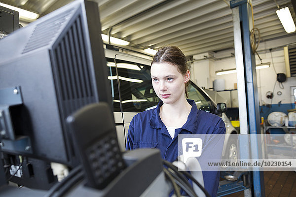 Young woman in repair garage checking car with electronic control