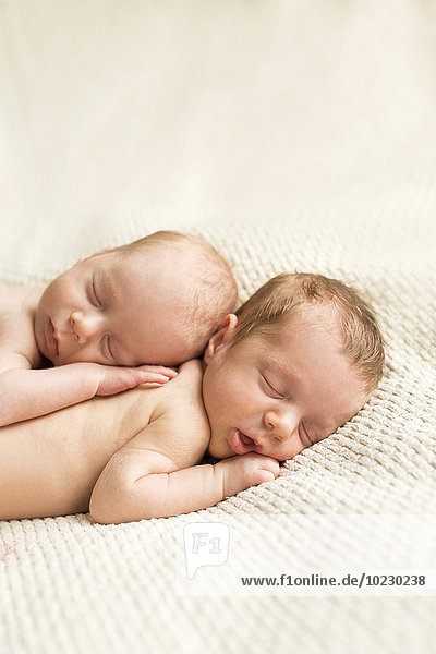 Newborn twins sleeping on blanket