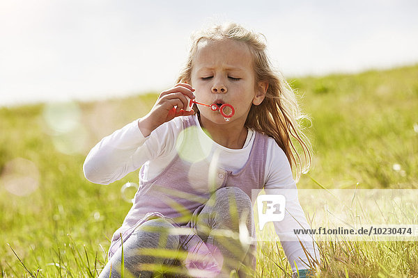 Porträt eines kleinen Mädchens  das Seifenblasen auf einer Wiese bläst.