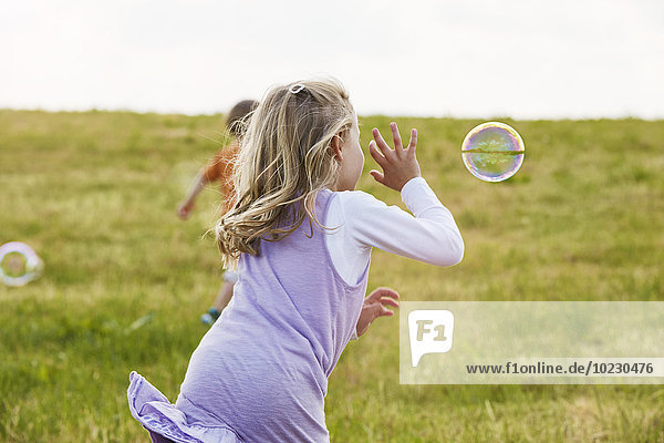 Little girl trying to catch soap bubbles on a meadow