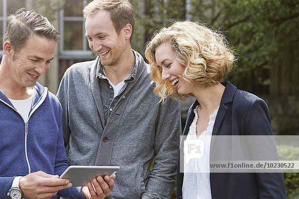 Drei glückliche Freunde im Freien  die sich ein digitales Tablett teilen.