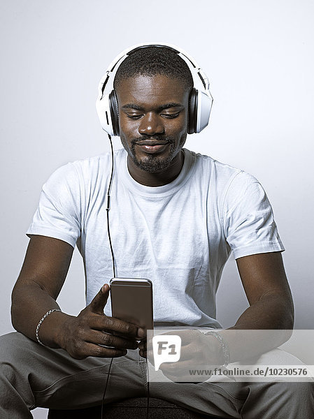 Lächelnder junger Mann mit Kopfhörer beim Blick aufs Handy