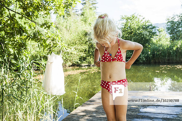 Girl in bikini standing on jetty at a lake