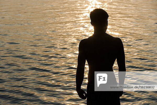 Silhouette eines Teenagers vor einem See bei Gegenlicht