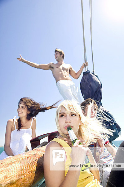 Junge Frau mit Bierflasche und Freunden auf einem Segelschiff