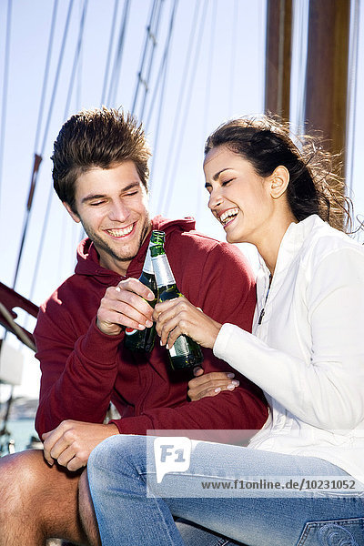 Happy young man and woman clinking beer bottles on a sailing ship
