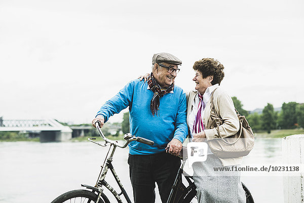 Happy senior couple standing at water's edge with bicycle