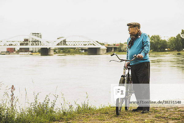 Älterer Mann mit dem Fahrrad am Wasser stehend