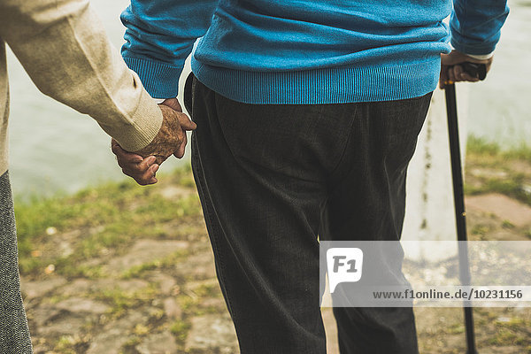 Senior couple holding hands at water's edge  close-up