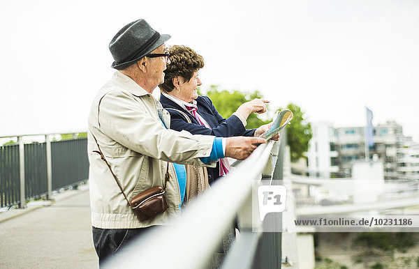 Senior couple with map standing on a bridge looking at view