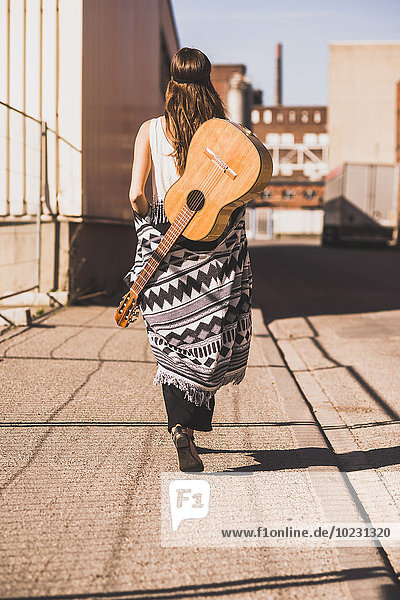 Junge Frau mit Gitarre auf dem Rücken  die auf der Straße geht