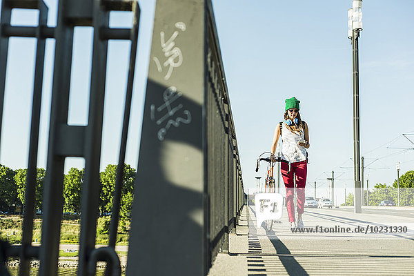Junge Frau mit Fahrrad auf dem Bürgersteig mit Blick auf das Handy