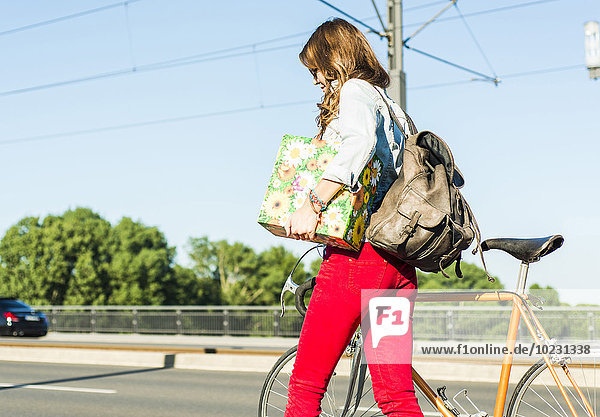 Junge Frau mit Fahrrad auf der Straße mit Geschenkbox