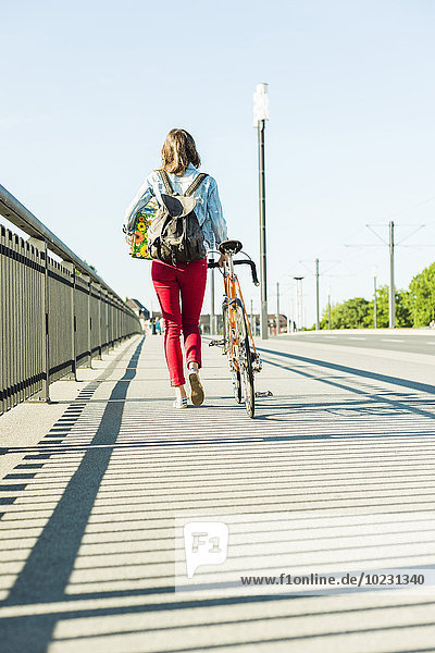 Junge Frau mit Fahrrad auf dem Bürgersteig mit Geschenkbox