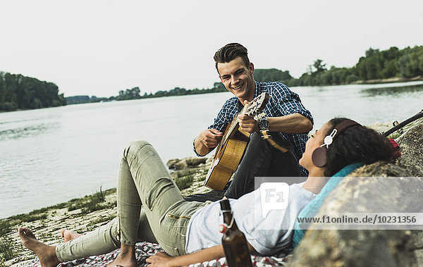 Relaxed young couple with guitar by the riverside