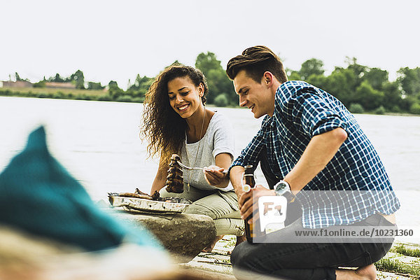 Glückliches junges Paar beim Grillen am Flussufer