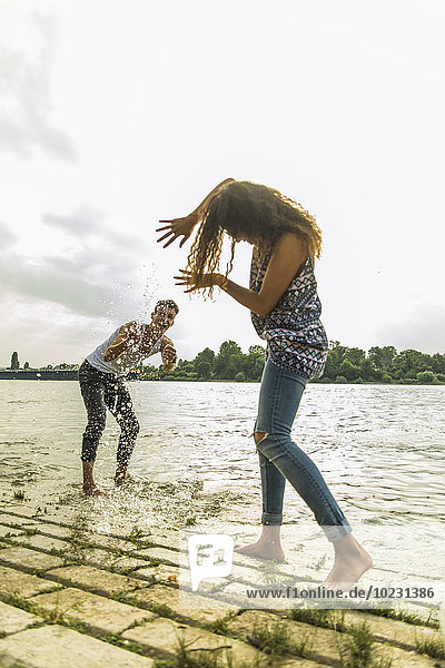 Verspieltes junges Paar  das mit Wasser am Flussufer plätschert.