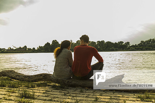 Junges Paar auf einem Baumstamm am Flussufer sitzend